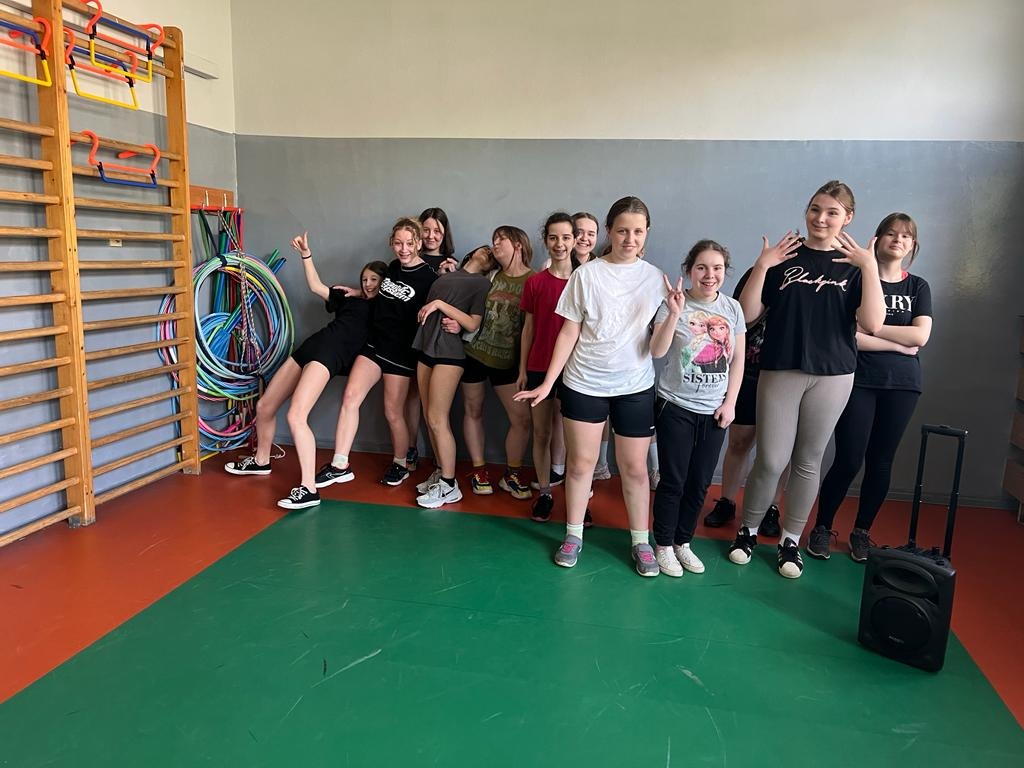 Grupa dziewczynek uśmiecha się do zdjęcia na sali gimnastycznej.