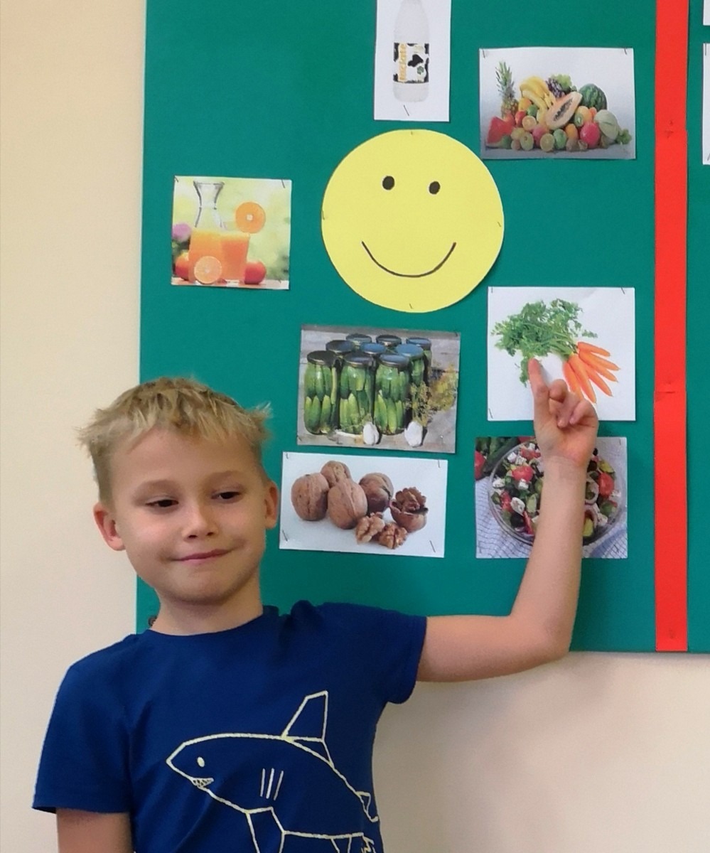 Chłopiec stojący przy tablicy z ilustracjami zdrowej żywności.