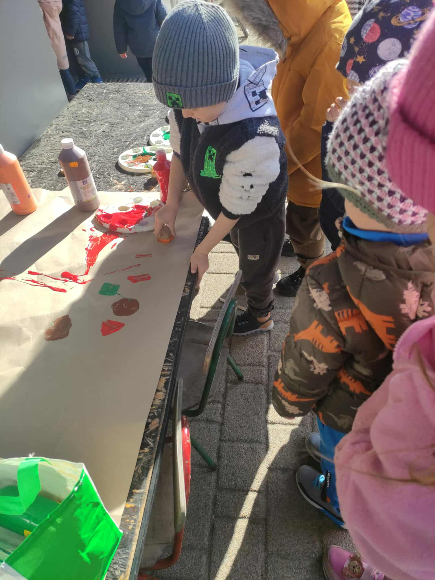 dzieci stoja na ogrodzie i robia pieczatki z ziemniakow