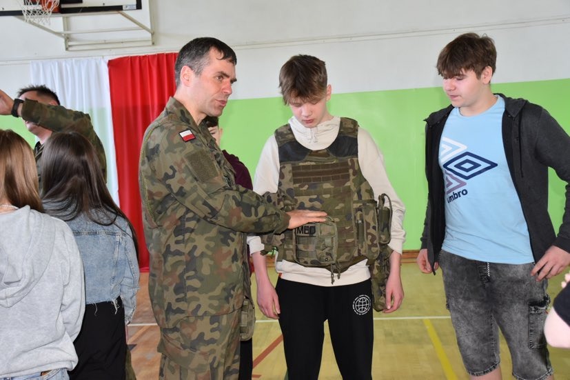 Żołnierz pokazuje i wyjaśnia uczniom sposób zakładania kamizelki kuloodpornej