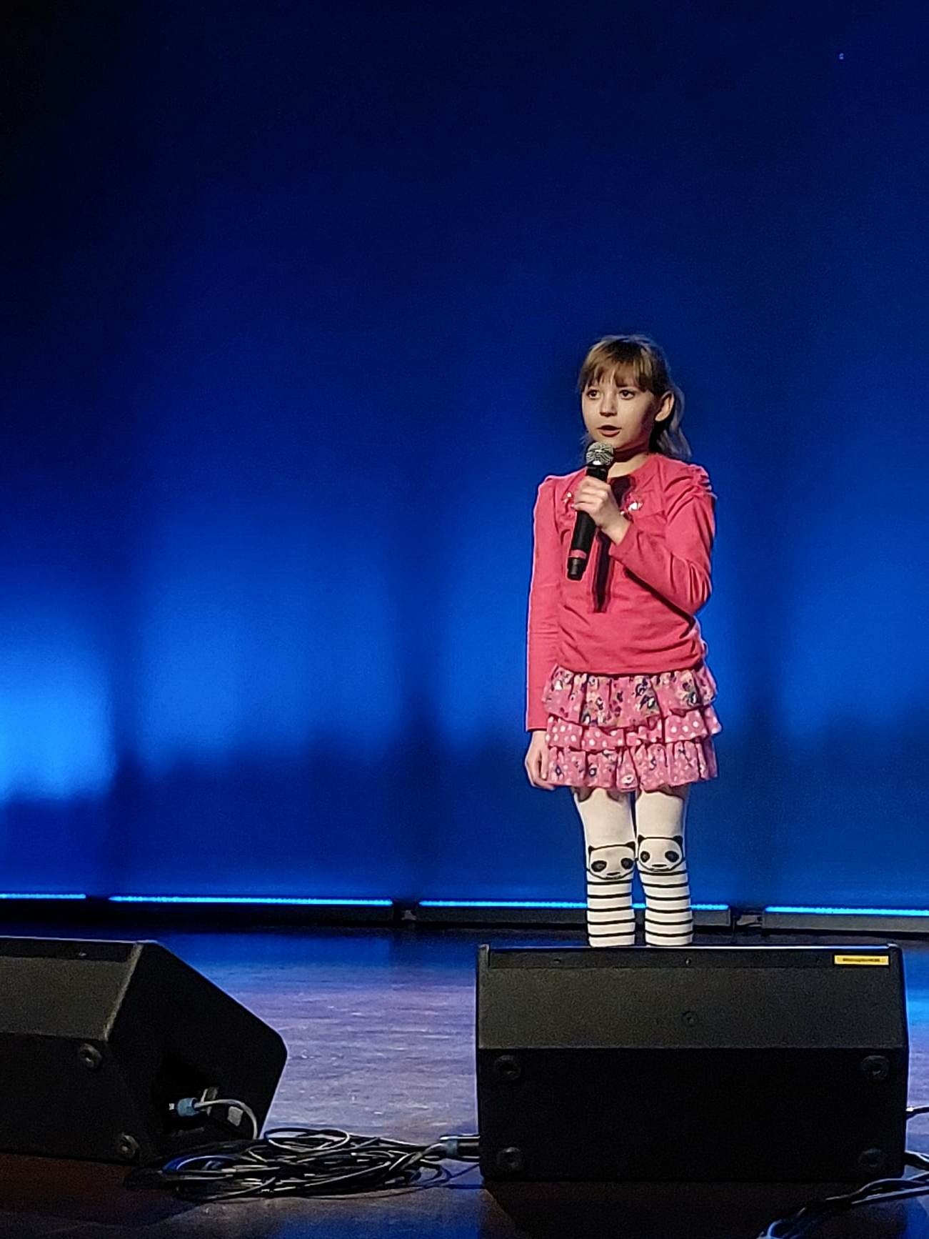 Dziewczynka z mikrofonem w ręku na scenie śpiewa piosenkę