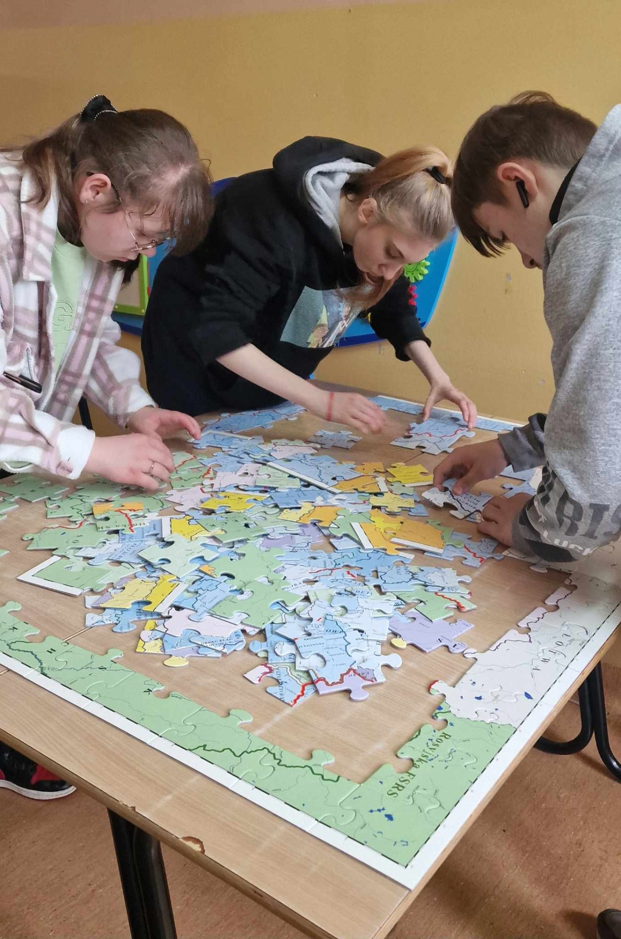3 uczniów przy stoliku układa z puzzli mapę