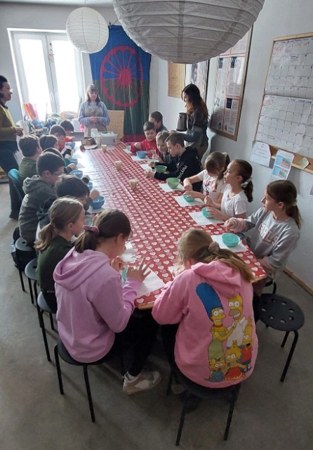 17 uczniów siedzi przy stole. Mają prze sobą kolorowe miski.