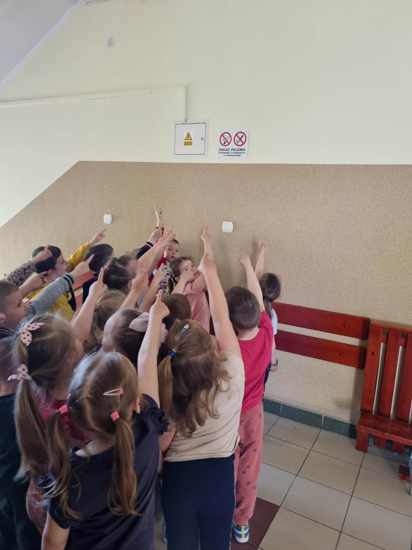 Grupa dzieci pokazuje znaki zakazu palenia, wiszące na szkolnym korytarzu