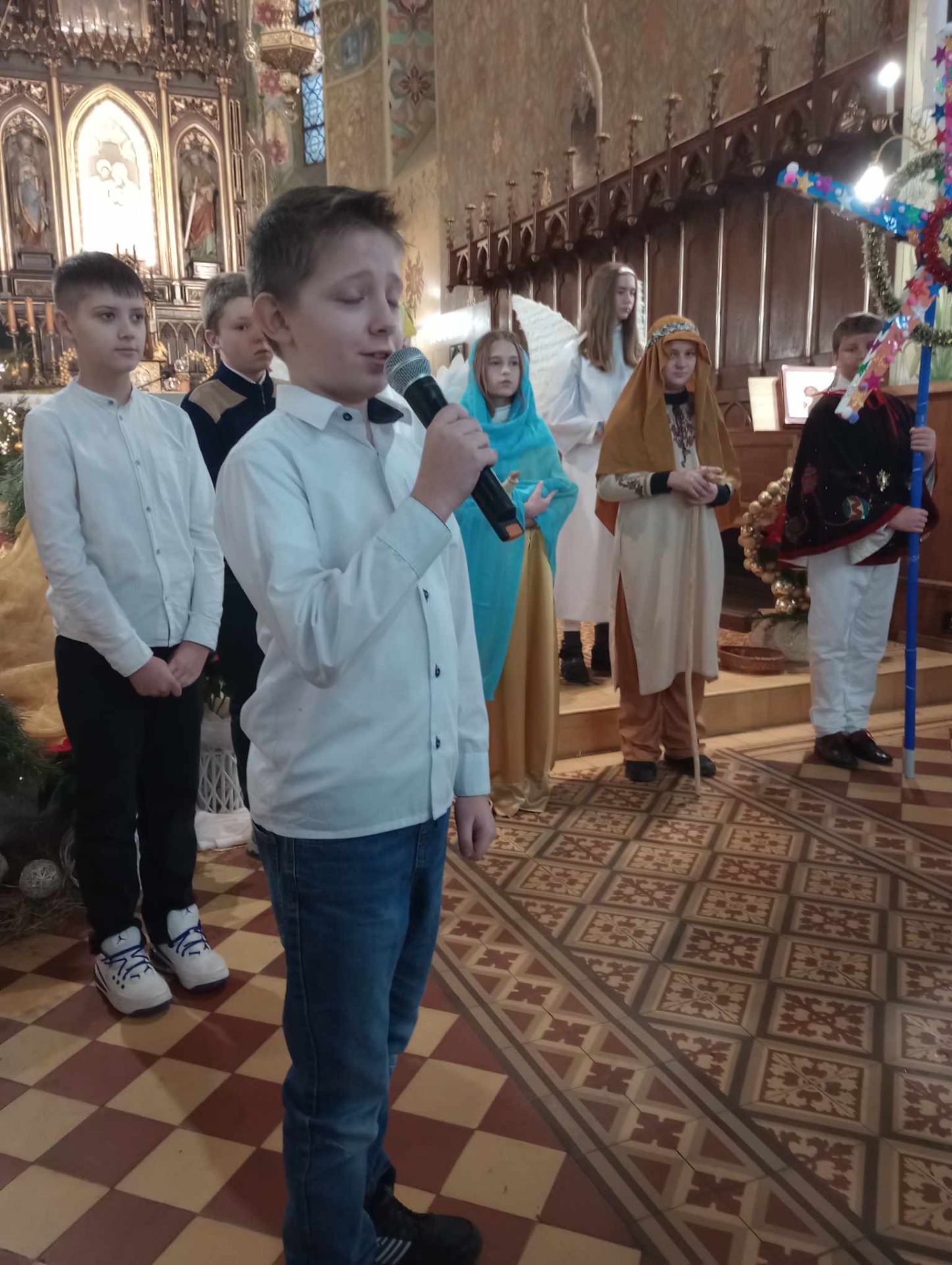 Zdjęcie przedstawia uczniów stojących w kościele przebranych za kolędników, Maryję, Józefa, aniołki, dzieci z Polski i Kolumbii biorących udział w przedstawieniu.